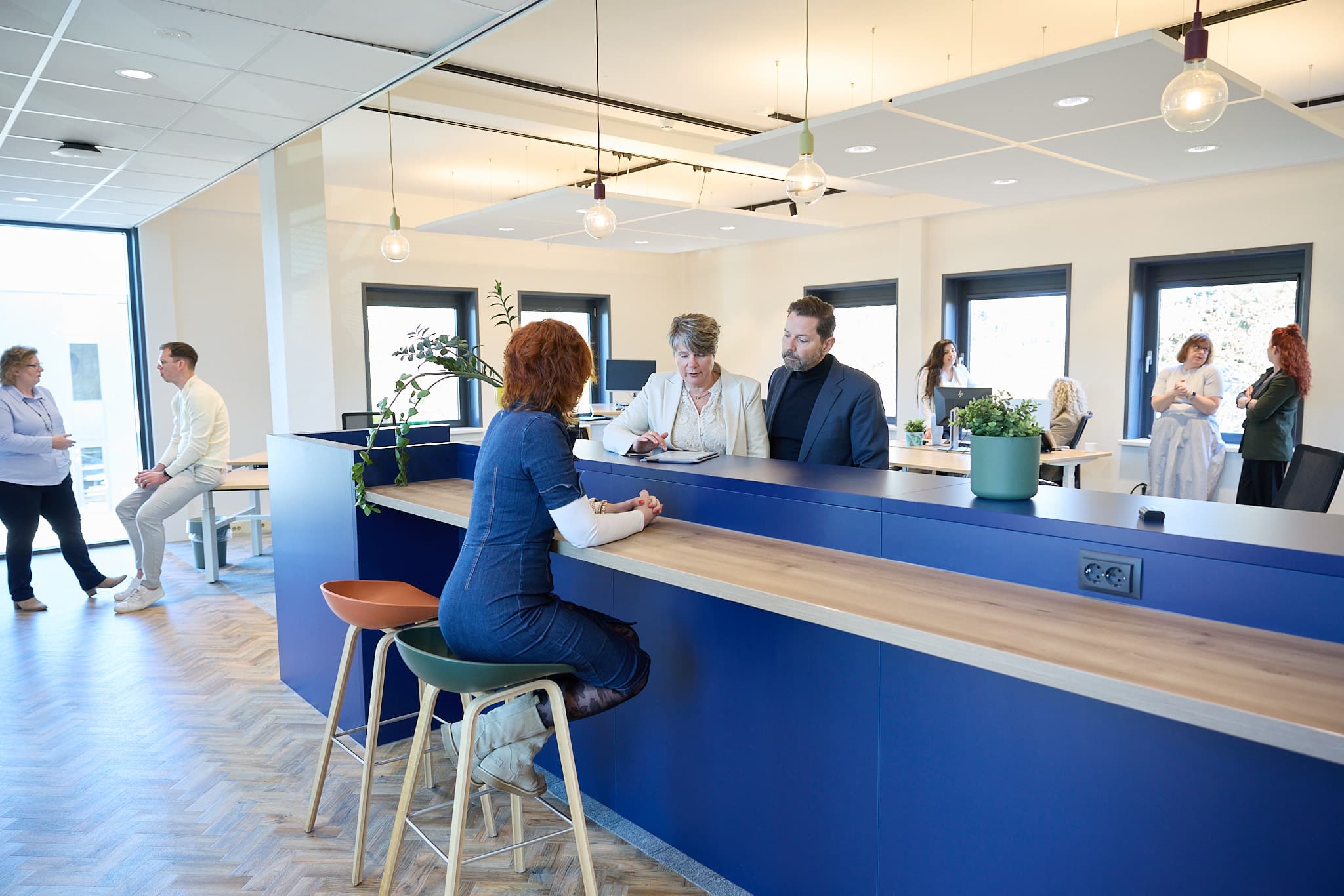 Drie arbeidsdeskundigen van Staatvandienst AD bespreken een casus rond een hoge tafel in lichte kantoorruimte.